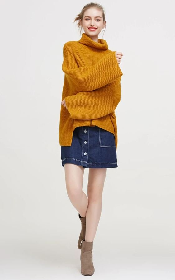 Woman in a mustard knit top with a denim mini skirt and ankle boots