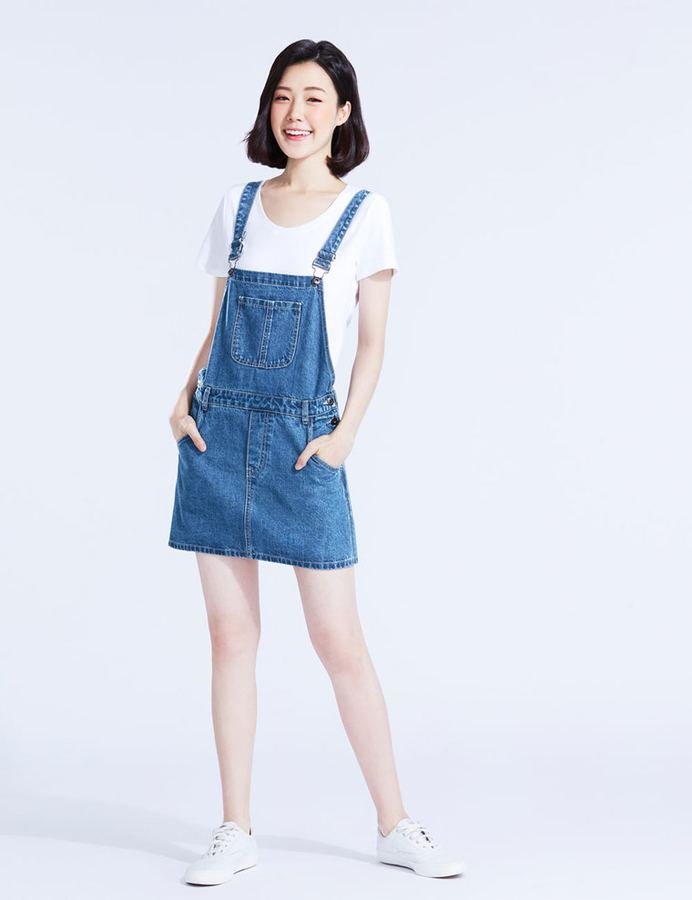 Woman in a denim pinafore dress layered over a tee
