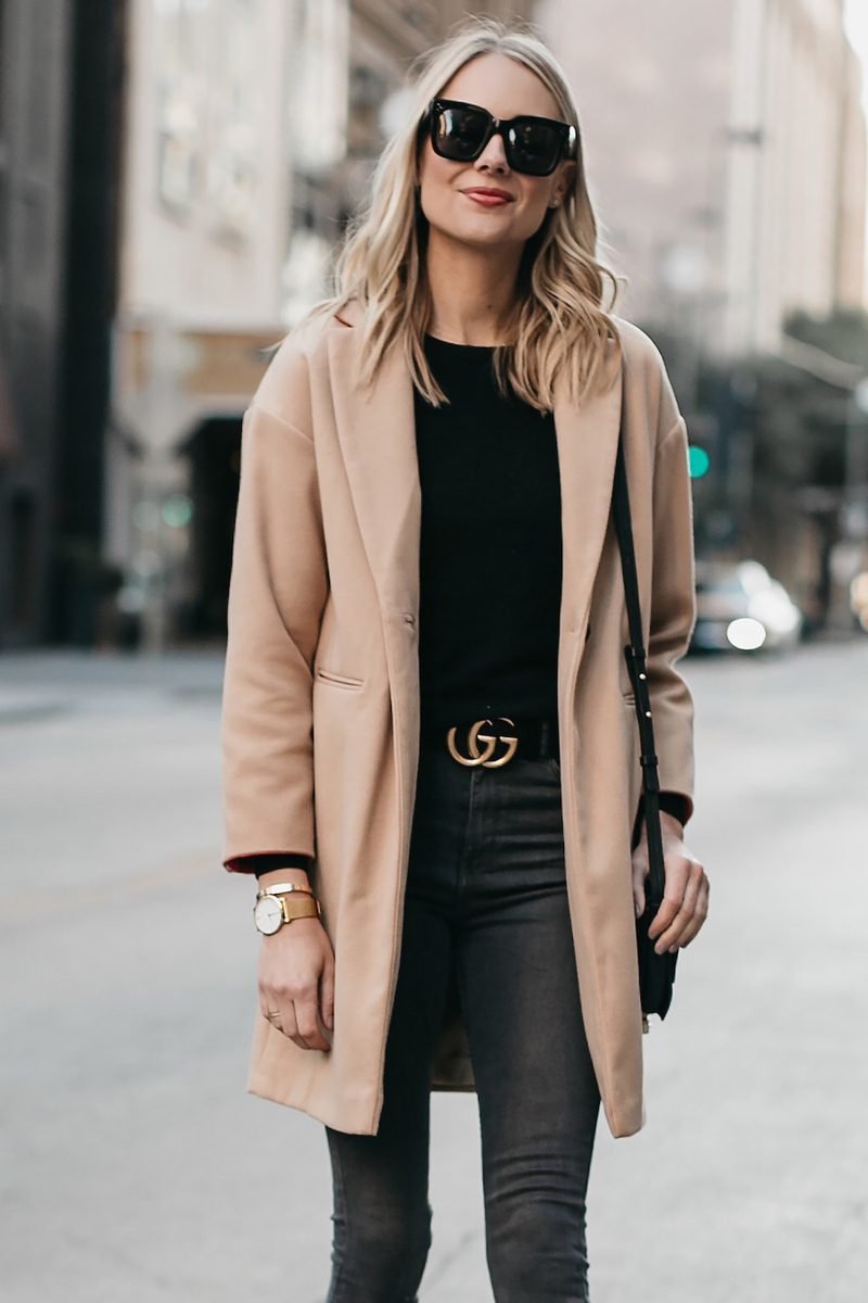 woman in camel coat over black top and dark jeans walking in the city at night