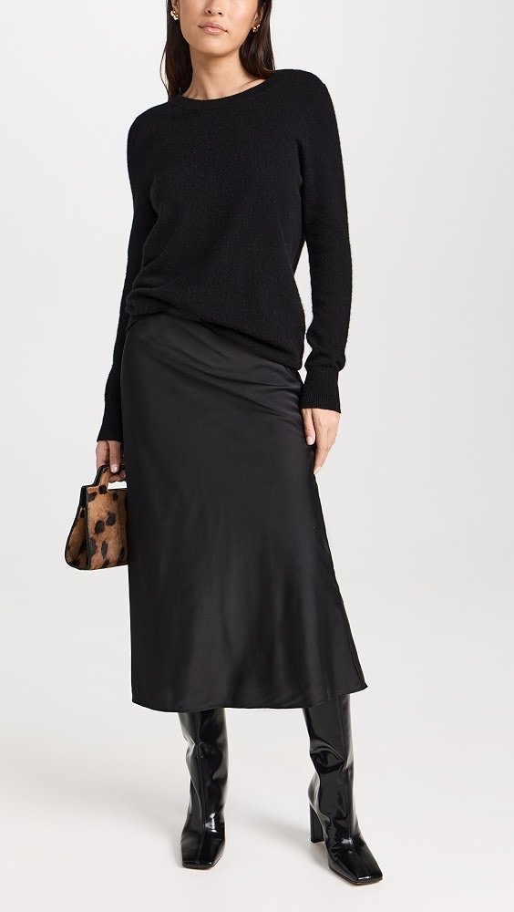 woman in champagne satin midi skirt and fitted black sweater at a wine bar